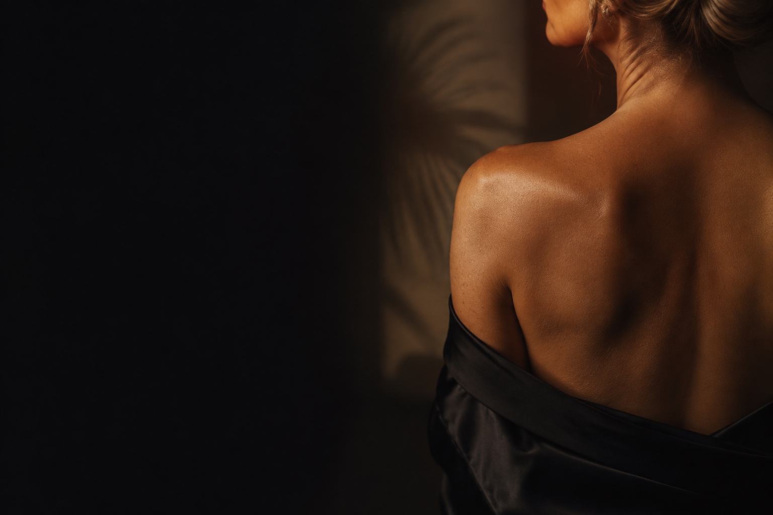 Woman with a warm, even spray tan seen from behind in soft lamplight